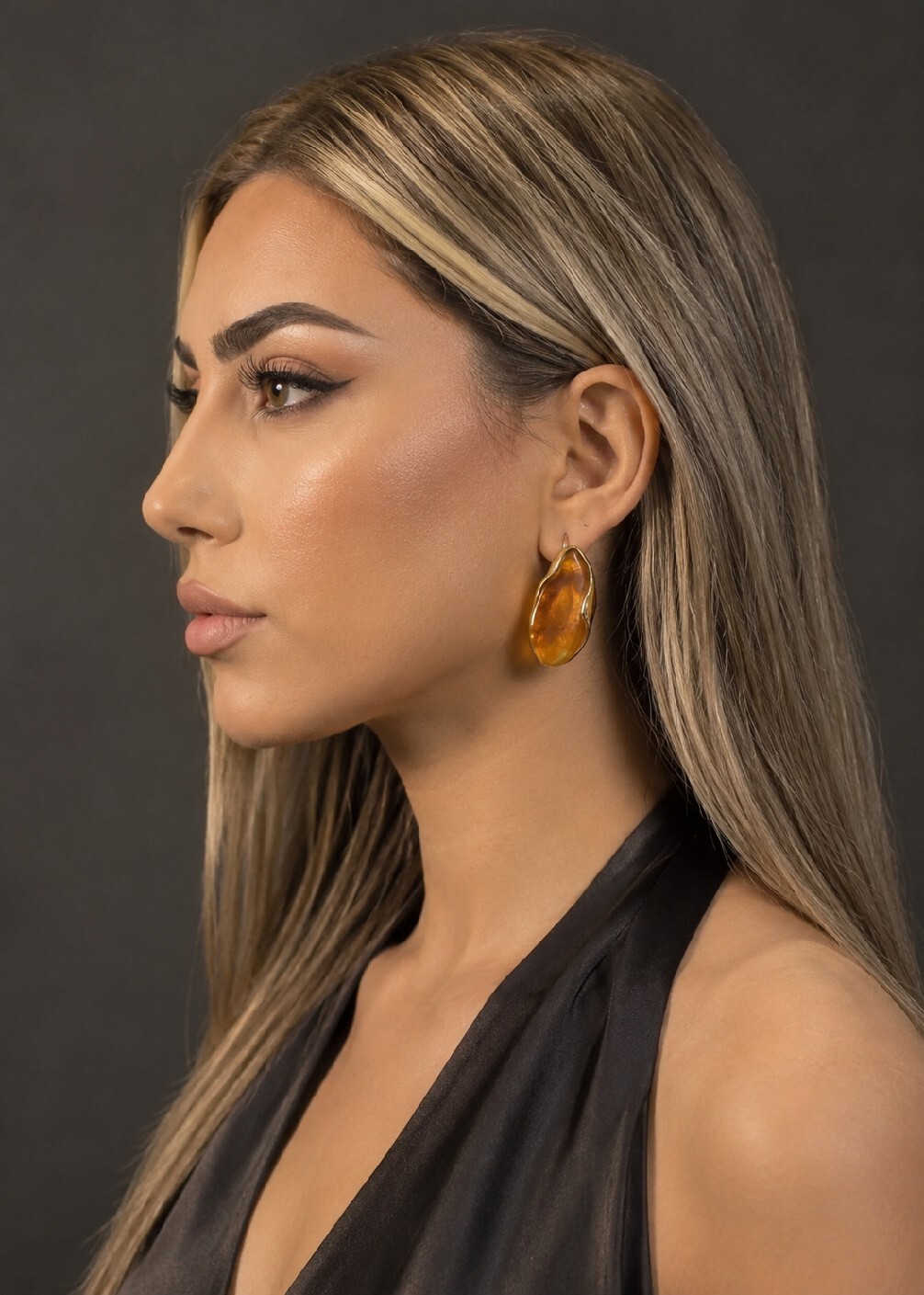 نمای نزدیک از گوشواره رزینی طرح سنگ (رنگ عسلی) با قاب طلایی Premium Collection در کنار دست