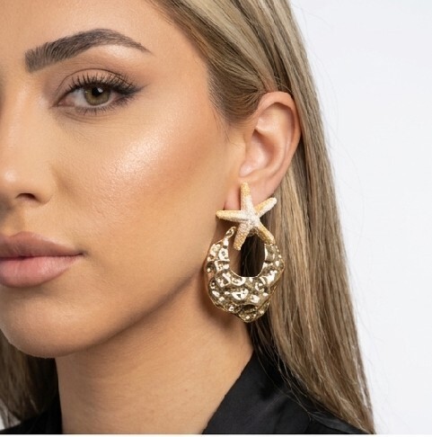 گوشواره بدلیجات زنانه رنگ ثابت با طراحی ستارهدریایی طلایی، روی صورت مدل با استایل شیک و لوکس